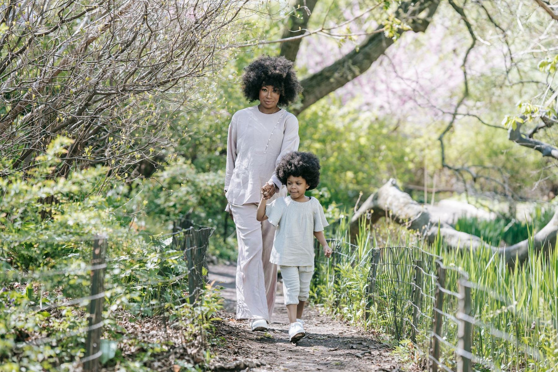 A mother and child walking hand in hand on a garden path